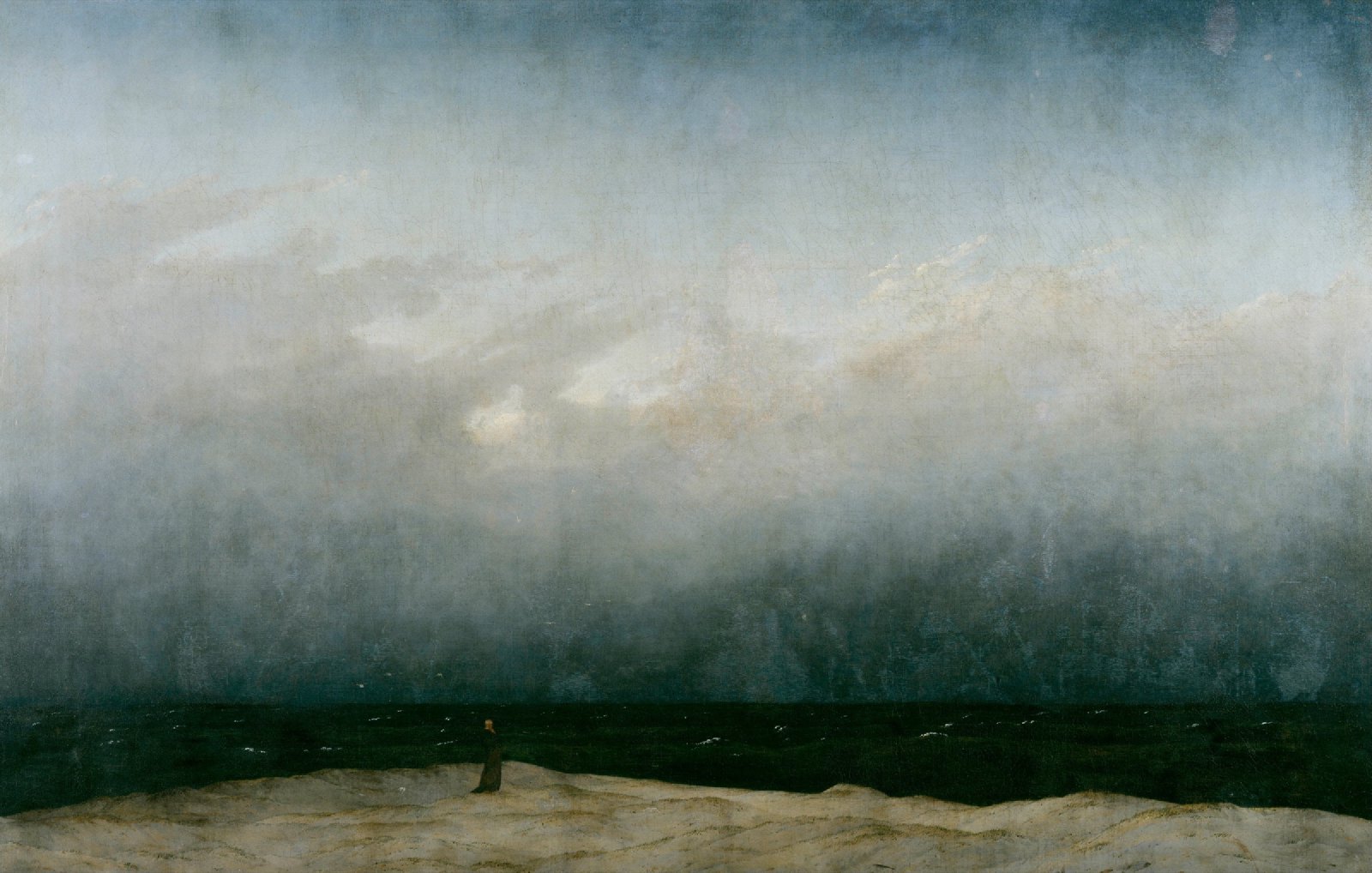 A solitary figure standing before a dark sea beneath an immense mist-filled sky